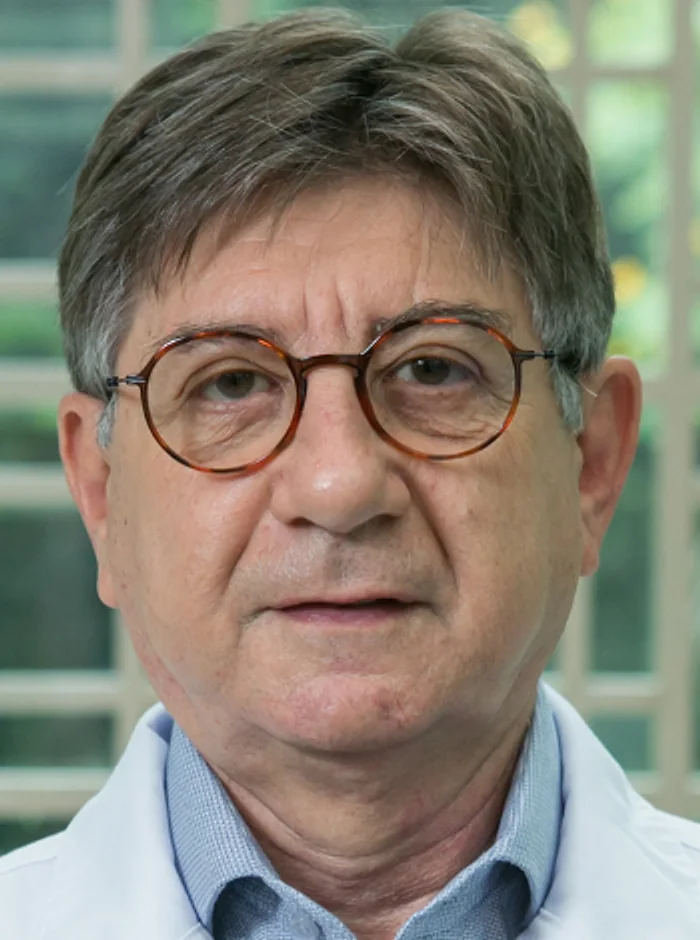 Rosto do Dr. Edmundo Kreisner, de óculos redondos de armação tartaruga, com a treliça clara e o jardim ao fundo
